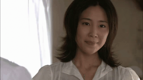 a woman wearing a white shirt and a necklace looks at the camera