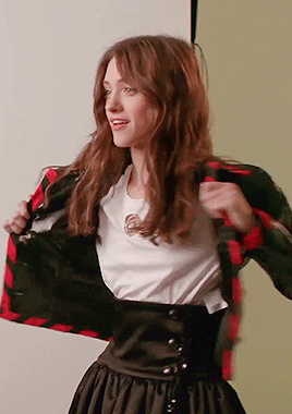 A Woman Wearing A White Shirt And A Plaid Jacket Takes Off Her Jacket GIF