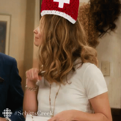 A Woman Wearing A White Shirt And A Red Hat With A Cross On It GIF