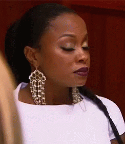 A Woman Wearing A White Shirt And Earrings Is Looking Down . GIF