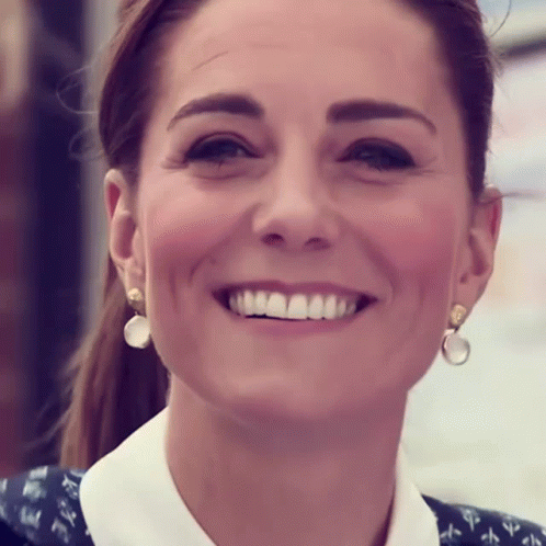 A Woman Wearing A White Shirt And Earrings Smiles For The Camera GIF