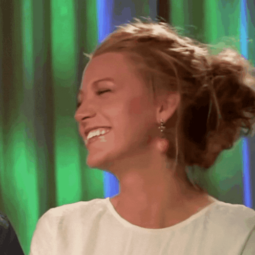 A Woman Wearing A White Shirt And Earrings Smiles With Her Eyes Closed GIF