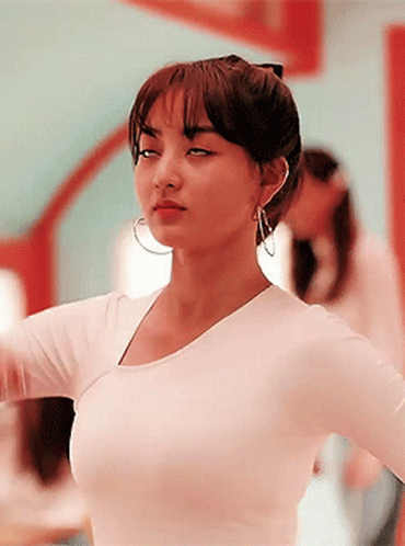 A Woman Wearing A White Shirt And Hoop Earrings Is Standing In Front Of A Mirror GIF