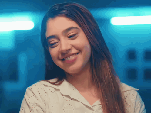 A Woman Wearing A White Shirt Is Smiling And Looking At The Camera GIF