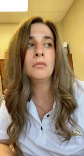 A Woman Wearing A White Shirt With A Gold Embroidered Letter T On The Front GIF