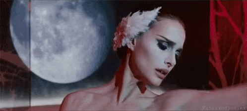 A Woman Wearing A White Swan Feather In Her Hair Is Dancing In Front Of A Full Moon . GIF