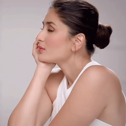 A Woman Wearing A White Tank Top Has Her Hand On Her Chin GIF
