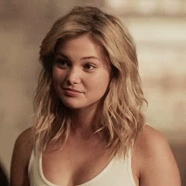 A Woman Wearing A White Tank Top Looks At The Camera GIF