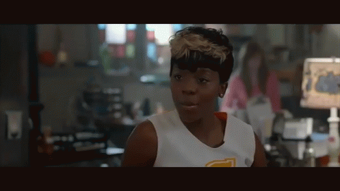A Woman Wearing A White Tank Top With A Yellow Letter T On The Front GIF