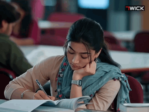 A Woman Wearing A Wick Watch Is Sitting At A Desk GIF