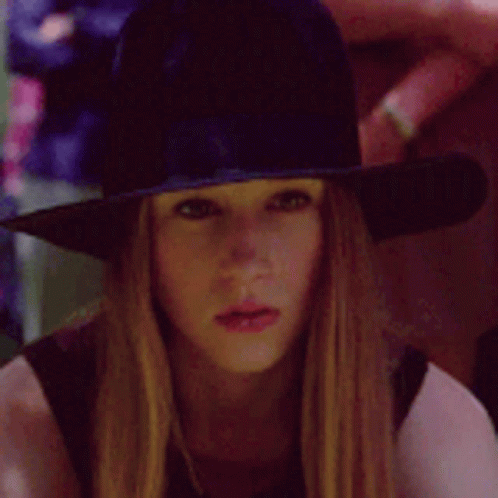 A Woman Wearing A Witch Hat Is Looking At The Camera GIF