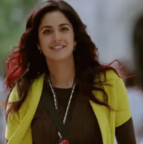 A Woman Wearing A Yellow Cardigan And A Lanyard Is Smiling . GIF