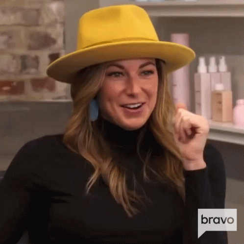 A Woman Wearing A Yellow Hat And A Black Turtleneck Is Talking To Someone . GIF