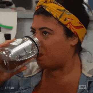 A Woman Wearing A Yellow Headband Is Drinking From A Clear Bottle .. GIF