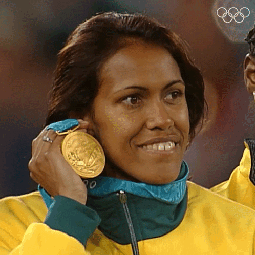 A Woman Wearing A Yellow Jacket Is Holding A Gold Medal Around Her Neck GIF