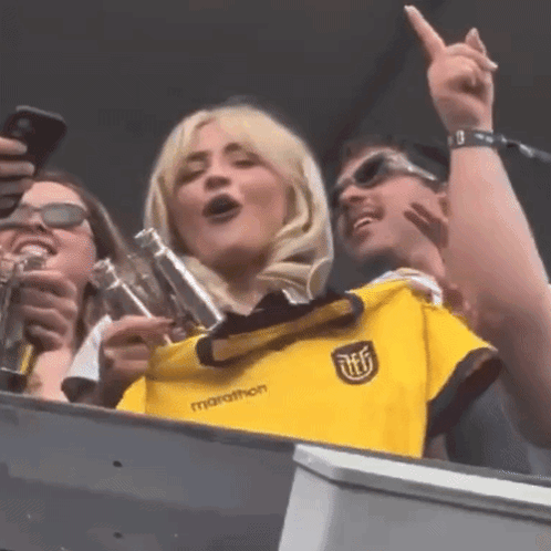 A Woman Wearing A Yellow Marathon Shirt Is Singing GIF