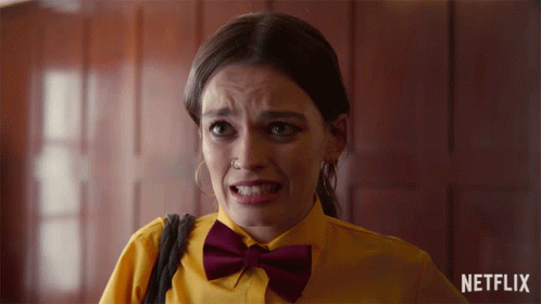 A Woman Wearing A Yellow Shirt And A Burgundy Bow Tie With A Netflix Logo In The Background GIF