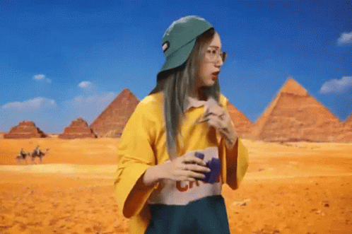 A Woman Wearing A Yellow Shirt And A Green Hat Is Standing In Front Of Pyramids . GIF