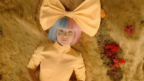 A Woman Wearing A Yellow Shirt And A Pink And Blue Bow On Her Head GIF