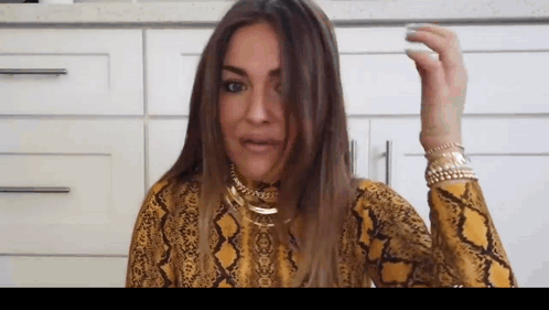 A Woman Wearing A Yellow Snake Print Shirt Is Holding Her Hair . GIF