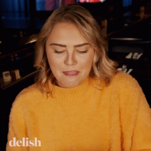A Woman Wearing A Yellow Sweater With The Word Delish On The Bottom Left GIF