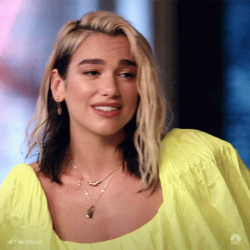A Woman Wearing A Yellow Top And A Necklace Is Making A Face . GIF