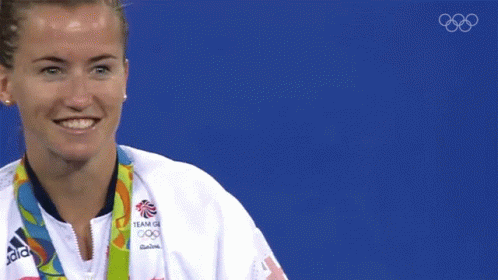 a woman wearing an adidas jacket is holding a gold medal in front of her face