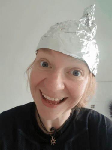 A Woman Wearing An Aluminum Foil Hat Smiles At The Camera GIF