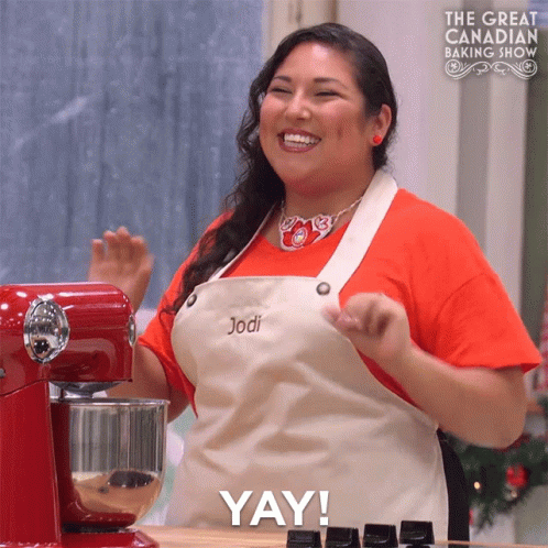 a woman wearing an apron with the name jodi on it stands in front of a red mixer