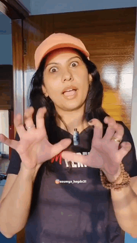 A Woman Wearing An Orange Hat Is Making A Funny Face With Her Hands GIF