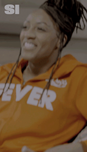 A Woman Wearing An Orange Hoodie With The Word Fever On It GIF