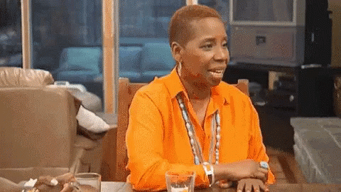 A Woman Wearing An Orange Shirt Is Sitting At A Table With A Glass Of Water . GIF