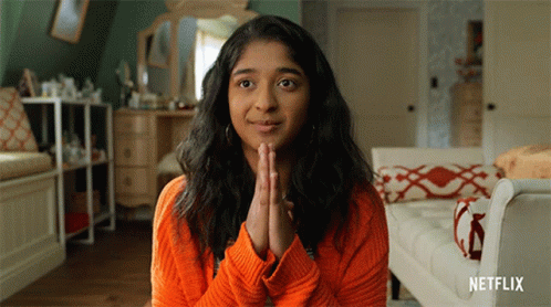 A Woman Wearing An Orange Sweater Is Praying With Her Hands Folded In Front Of Her Face .. GIF