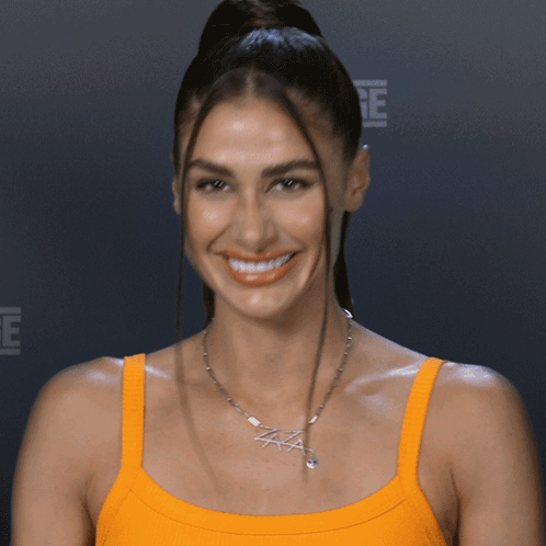 A Woman Wearing An Orange Tank Top And A Necklace That Says Aaa GIF