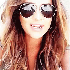 A Woman Wearing Aviator Sunglasses Is Smiling For The Camera . GIF