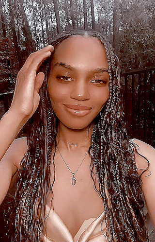 A Woman Wearing Braids And A Necklace Is Smiling For The Camera GIF