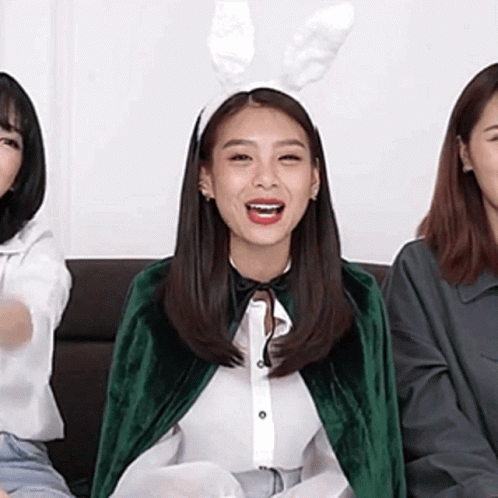 A Woman Wearing Bunny Ears And A Green Cape Is Sitting On A Couch With Two Other Women . GIF