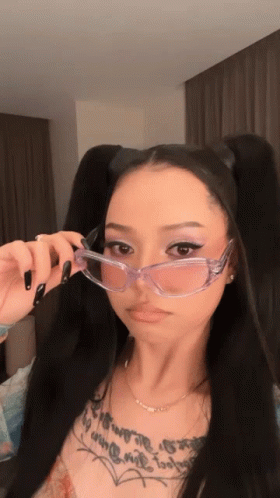 A Woman Wearing Clear Glasses Has A Tattoo On Her Chest GIF