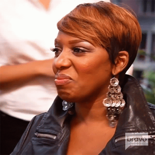A Woman Wearing Earrings And A Leather Jacket Has A Bravo Logo On Her Jacket GIF