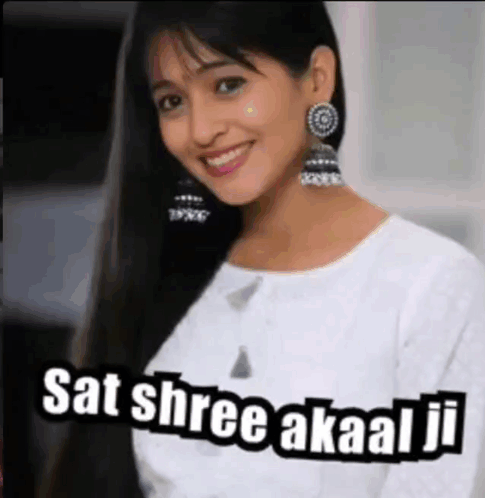 a woman wearing earrings and a white shirt is smiling and says sat shree akaal ji