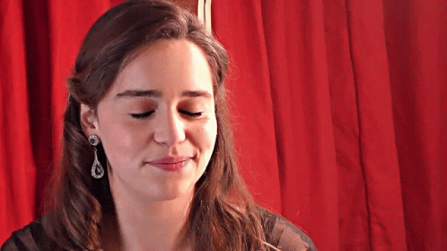 A Woman Wearing Earrings Is Smiling With Her Eyes Closed GIF