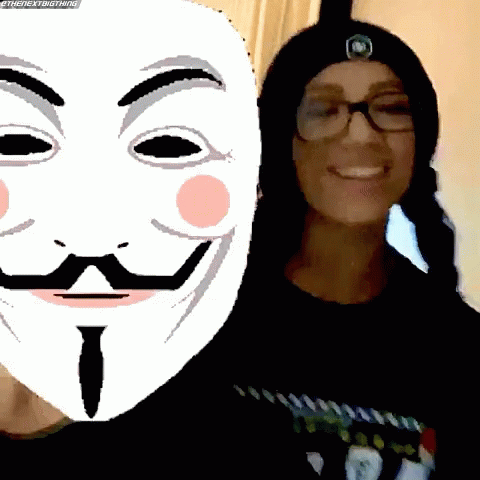 A Woman Wearing Glasses And A Beanie Stands Next To A Mask With A Mustache And Eyebrows GIF