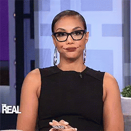 A Woman Wearing Glasses And A Black Dress Is Smiling And Making A Funny Face . GIF