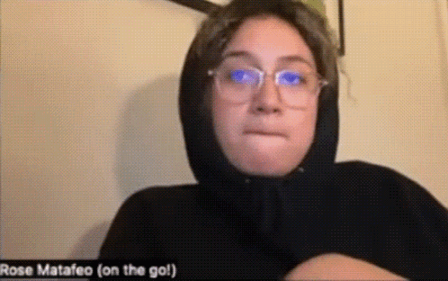 A Woman Wearing Glasses And A Black Hoodie Is Making A Face . GIF