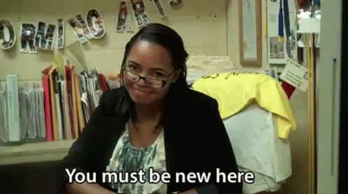 A Woman Wearing Glasses And A Black Jacket Is Sitting At A Desk And Smiling . GIF