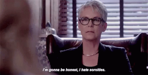 A Woman Wearing Glasses And A Black Jacket Is Sitting In A Chair And Talking To Someone . GIF