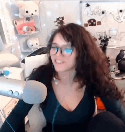 A Woman Wearing Glasses And A Black Shirt Is Sitting In Front Of A Microphone . GIF