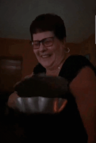 A Woman Wearing Glasses And A Black Shirt Is Smiling And Holding A Bowl GIF