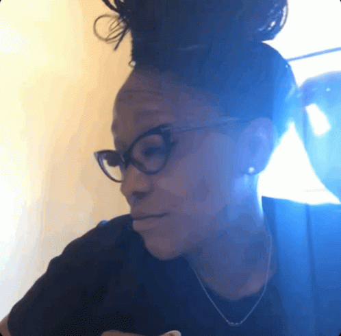 A Woman Wearing Glasses And A Black Shirt Looks Down At Something GIF