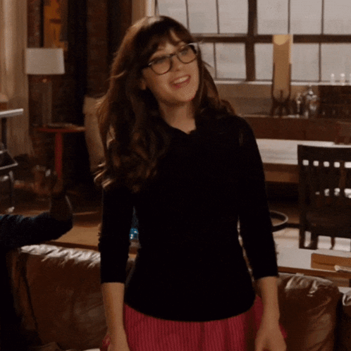 A Woman Wearing Glasses And A Black Shirt Stands In A Living Room GIF